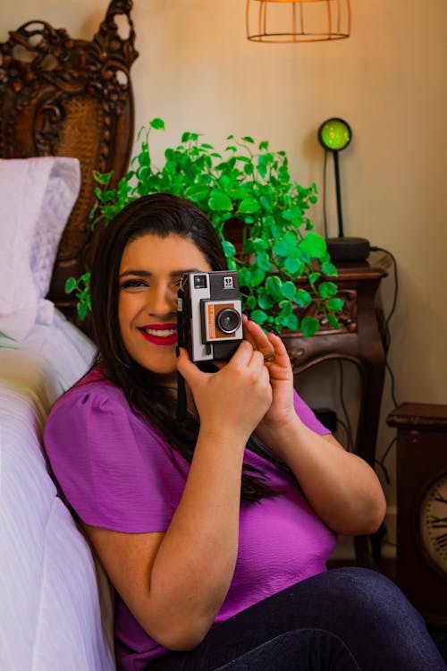 Young Woman Sitting next to the Bed and Taking a Picture with a Vintage Camera 