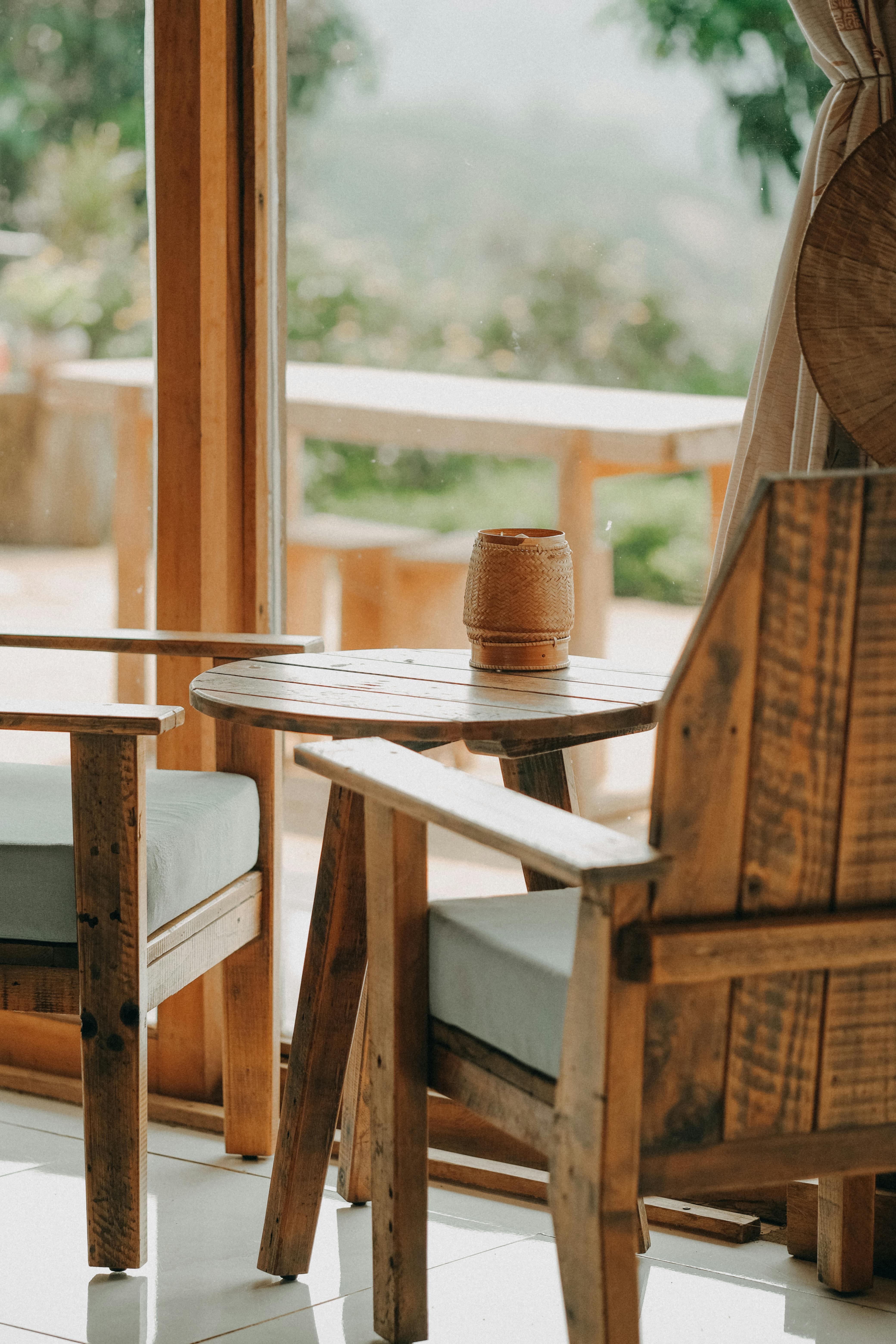 Rustic wooden armchairs and table in a sunlit room with outdoor view.