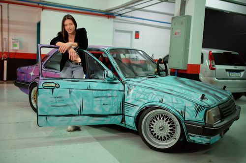 Free Woman posing confidently with a custom graffiti-painted car in an indoor garage setting. Stock Photo