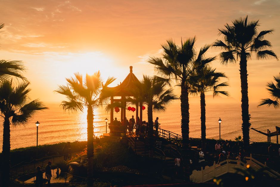 Silhouette of people and palm trees by a coastal gazebo at sunset in Lima, Peru.