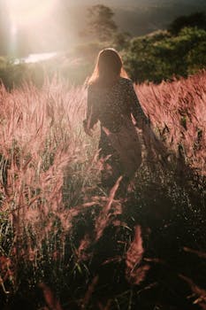 日落时分，一位年轻女子漫步在草地上，四周环绕着大自然的美丽