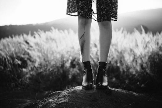 一张黑白照片，拍摄的是站在山上自然环境中的皮靴