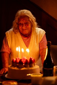 A senior adult woman joyfully celebrates her birthday with a cake and lit candles indoors.