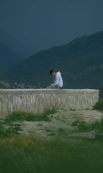 A man sits on a stone wall using a smartphone amid mountains in Yungay, Peru.