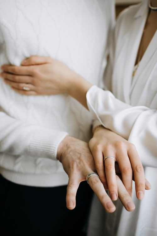 Free A touching close-up of a couple's hands and arms, showcasing wedding rings and elegant attire. Stock Photo