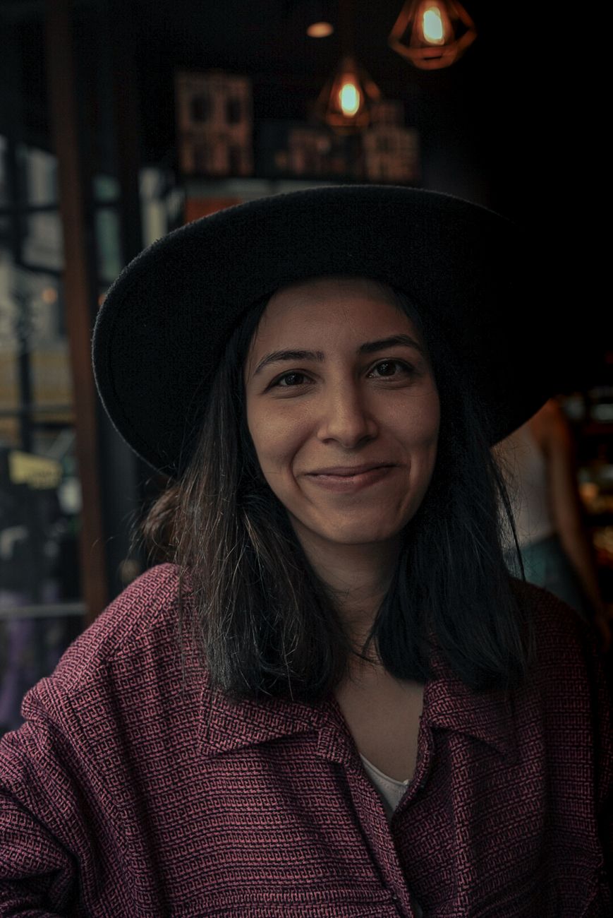 Young woman smiling indoors wearing a stylish hat. Warm and candid portrait lighting.