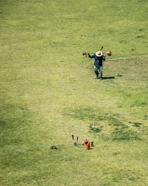High Angle Shot of a Man Walking on a Grass Field with a Grass Trimmer 