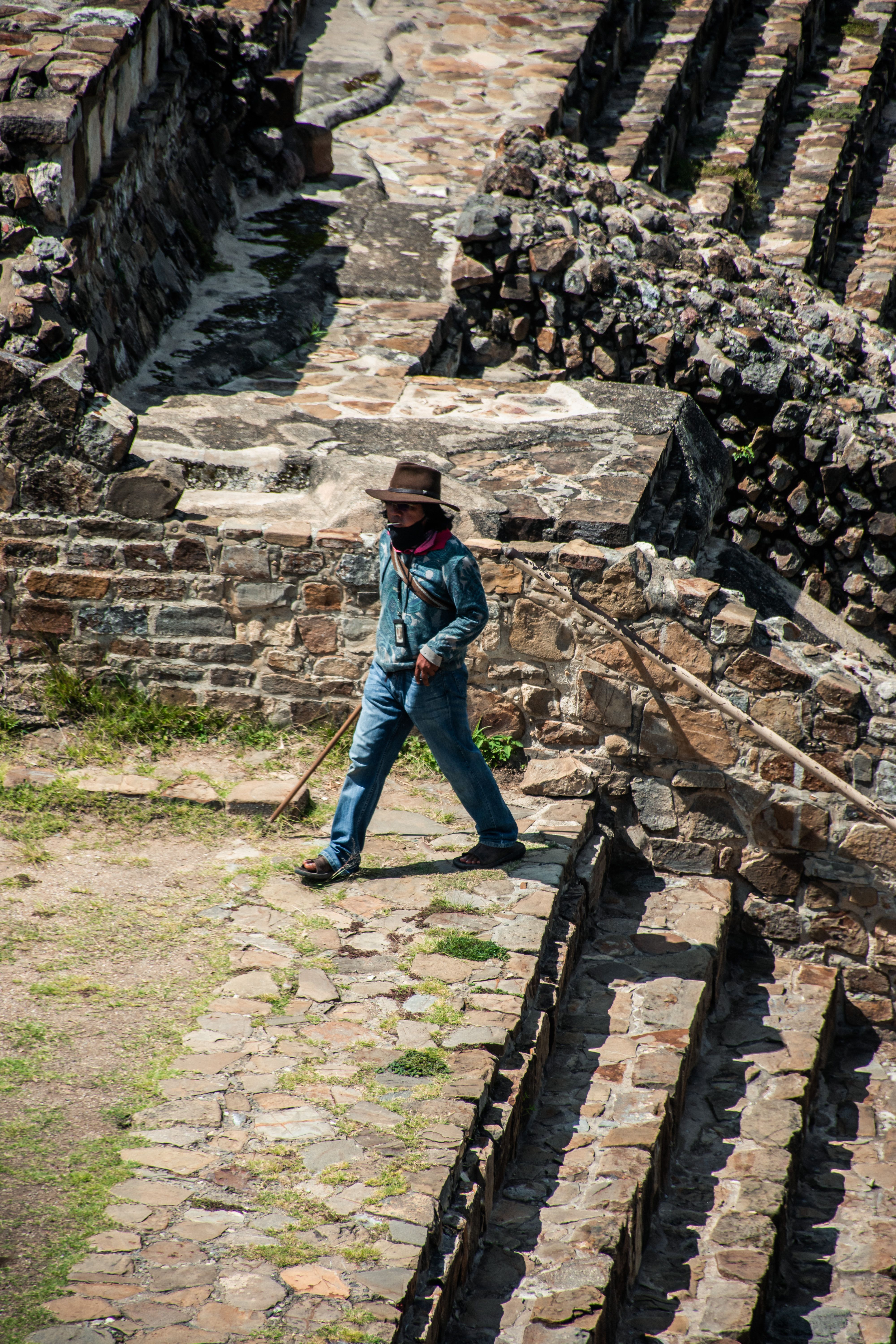 A man in a hat walks through sunlit ancient ruins, caught in a vertical shot.