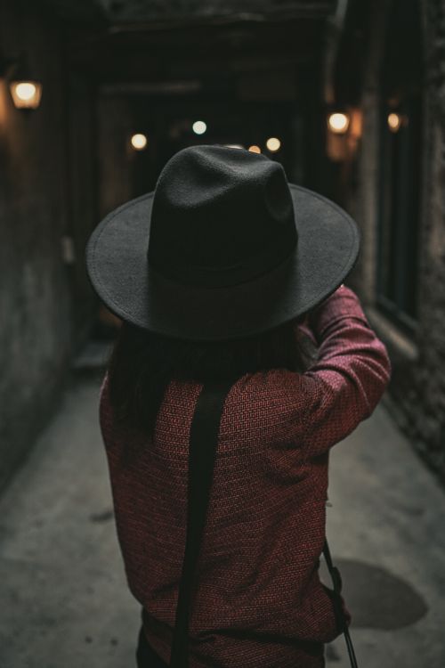 Free Person in a dark corridor wearing a stylish hat and red outfit, captured from behind. Stock Photo