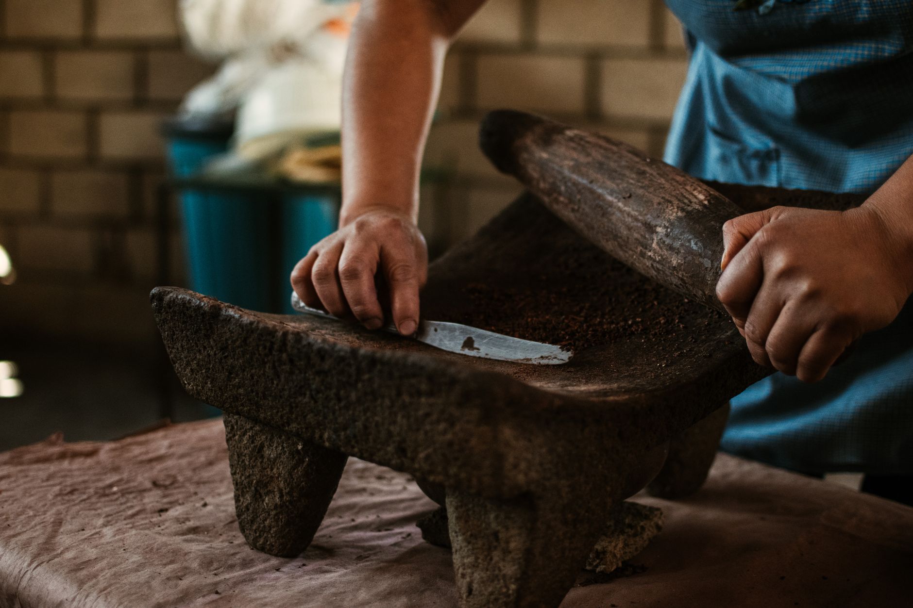 Close-up of hands using a stone metate for grinding in a traditional setting.