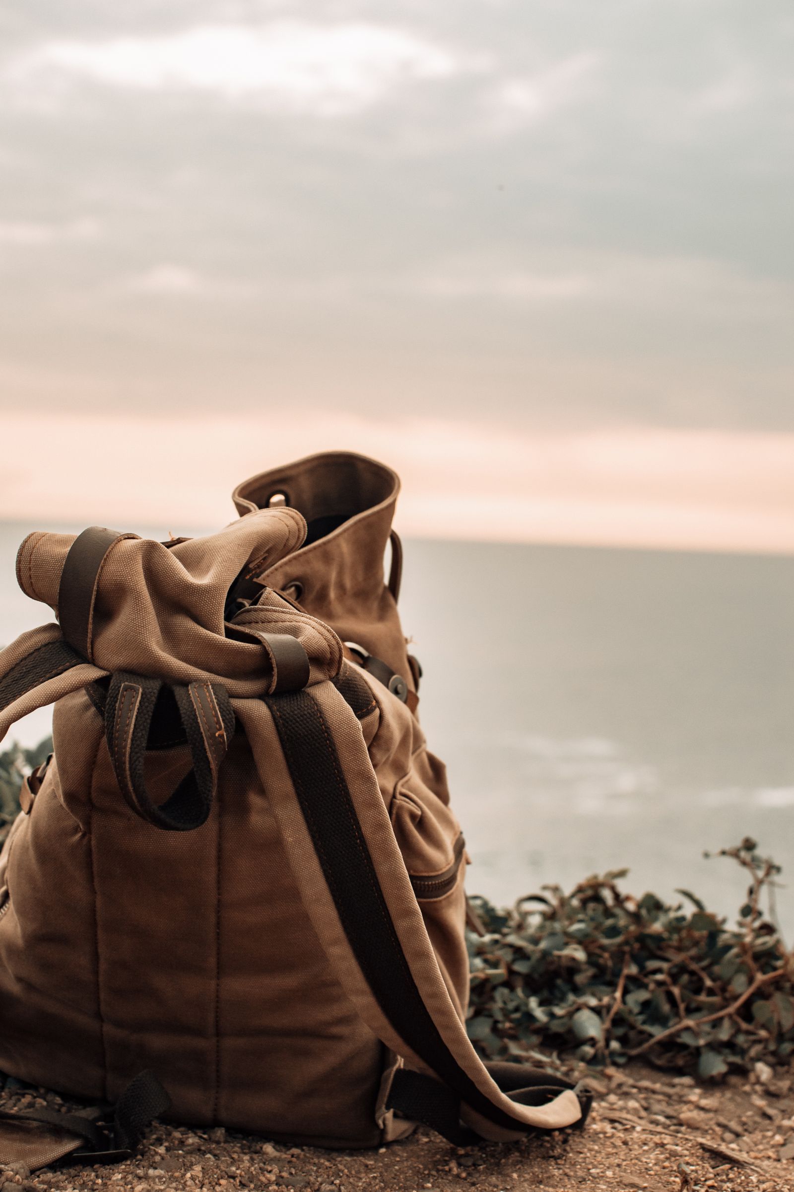 Brown waxed canvas backpack resting on a coastal cliff, weatherproof performance
