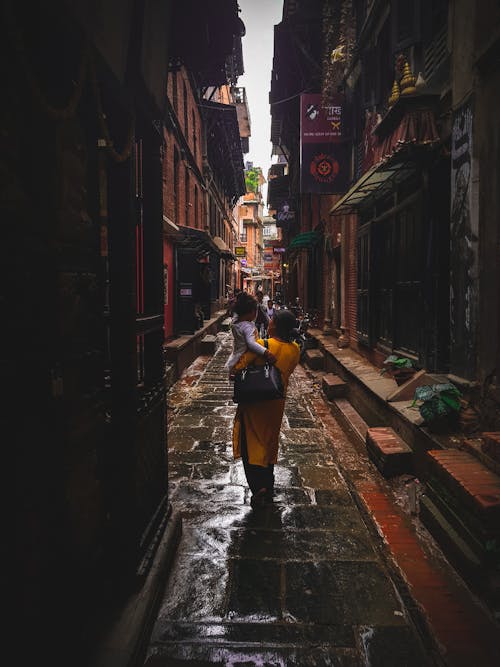 Woman Carrying Girl Between Concrete Building Durng Daytime