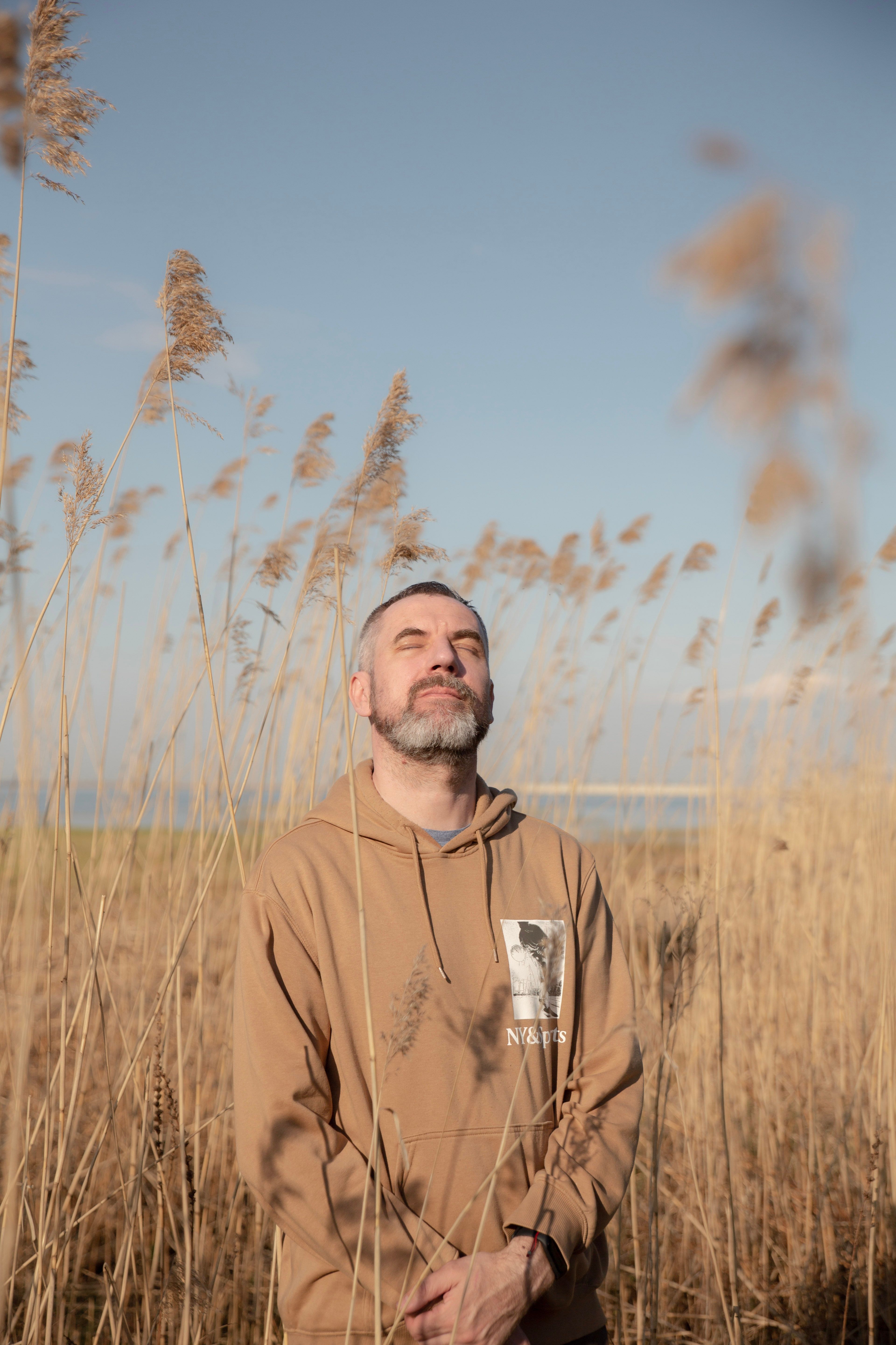 Man enjoying relaxation in a field, eyes closed under sunlight.