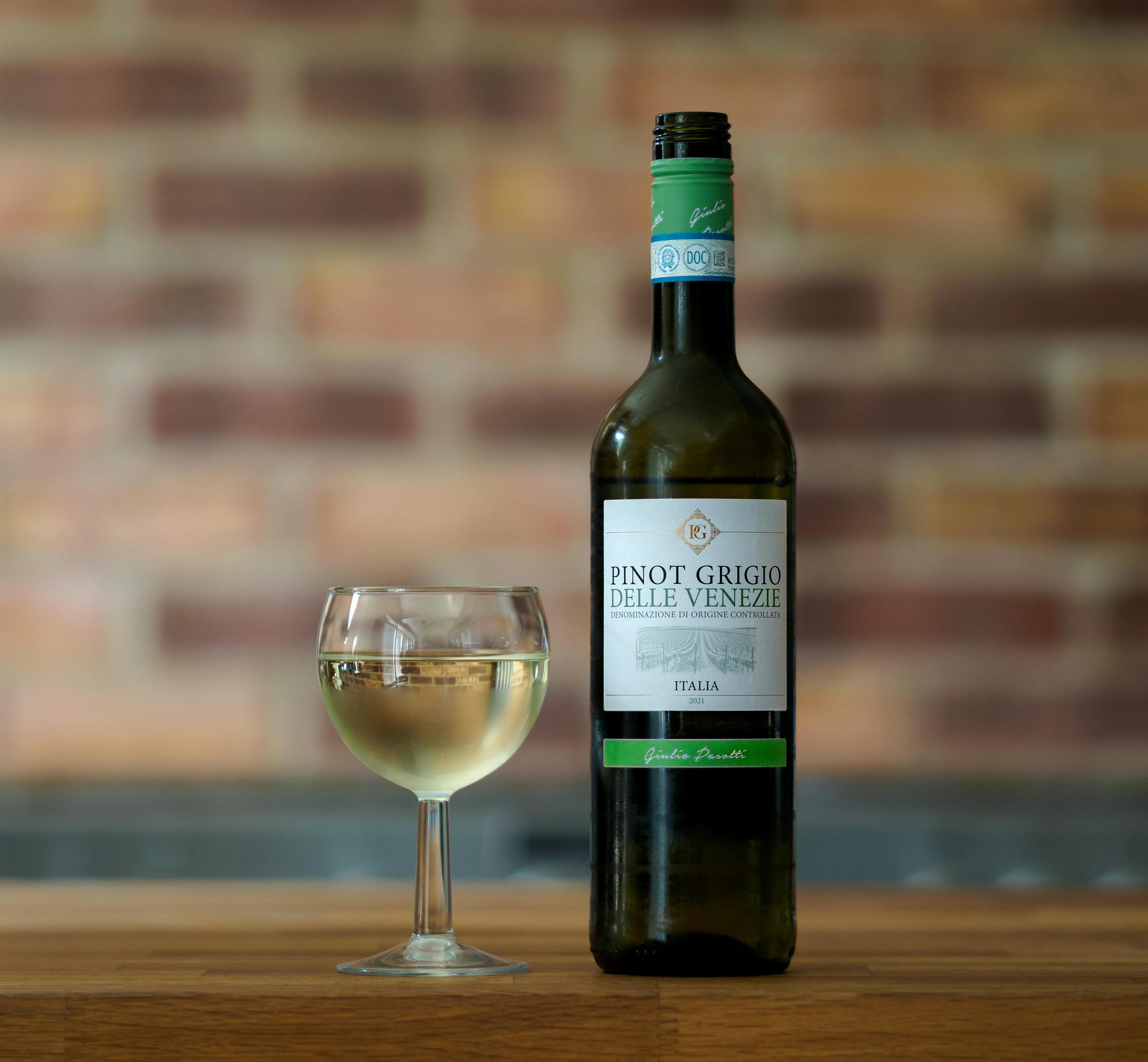 A bottle of Pinot Grigio and a filled glass on a wooden surface indoors.