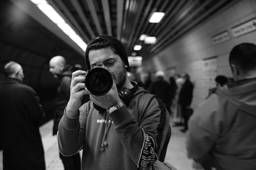 Black and White Picture of a Young Man with a Camera on a Crowded Subway Station 