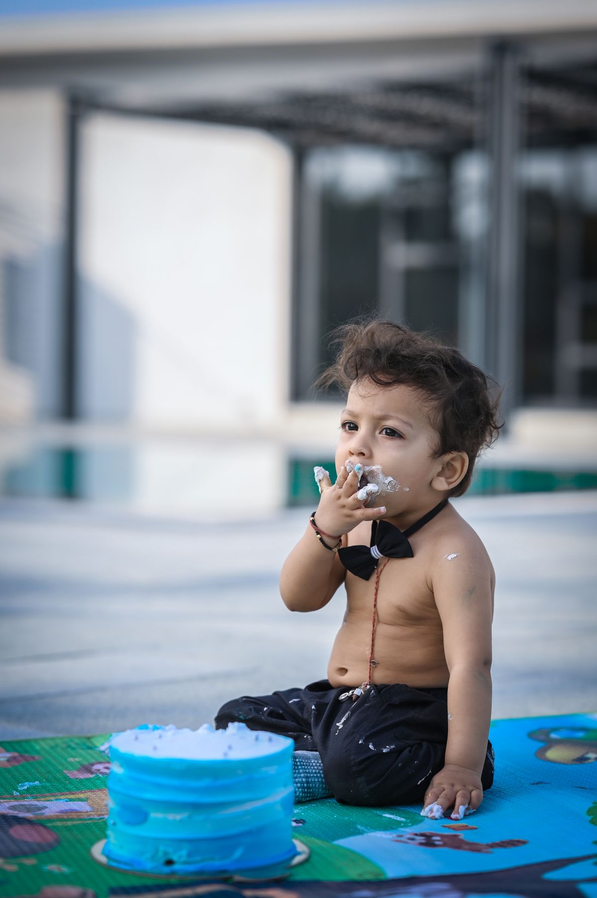 Cute toddler with cake on face during outdoor birthday celebration near pool. Stock Photo.