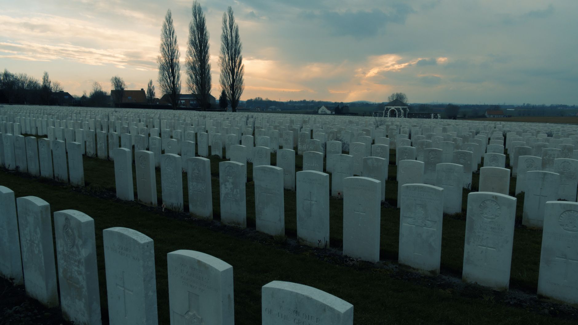 Rows of gravestones in a WWI cemetery in Flanders during sunset, reflecting solemn remembrance.