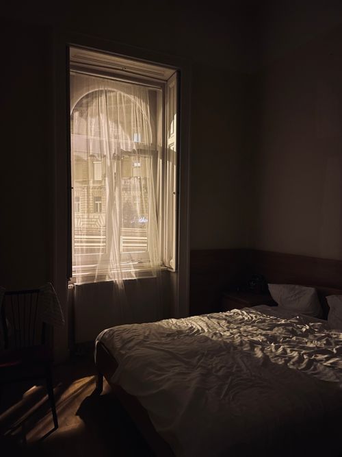 Free Sunlit window illuminating a cozy bedroom in Budapest, Hungary with elegant curtains and bedding. Stock Photo