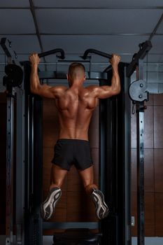 A muscular man performing a pull-up in a modern gym setting, showcasing strength and fitness.