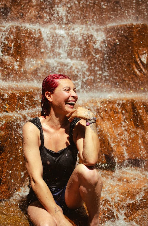 Woman Sitting under a Waterfall and Smiling 