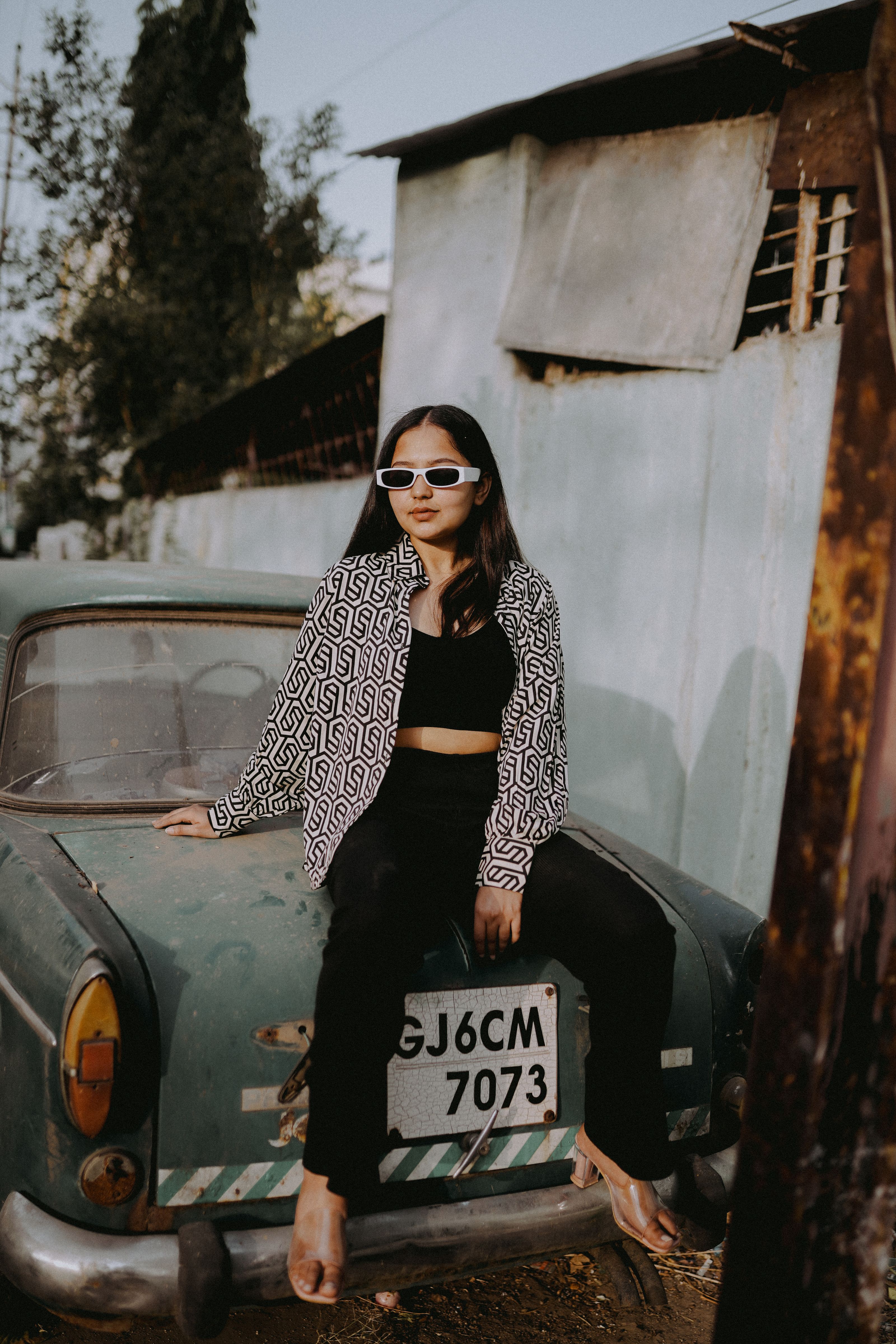 Jovem mulher em óculos escuros modernos posa com um carro clássico, exalando charme retrô.