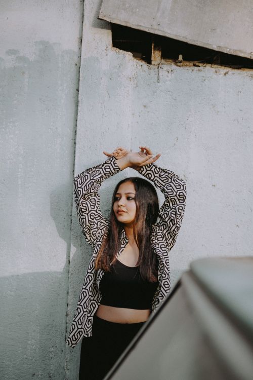 Free Stylish young woman posing with arms raised against a textured wall in an urban setting. Stock Photo
