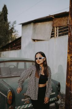Stylish woman in sunglasses stands by a retro car outside, exuding a cool, vintage vibe.