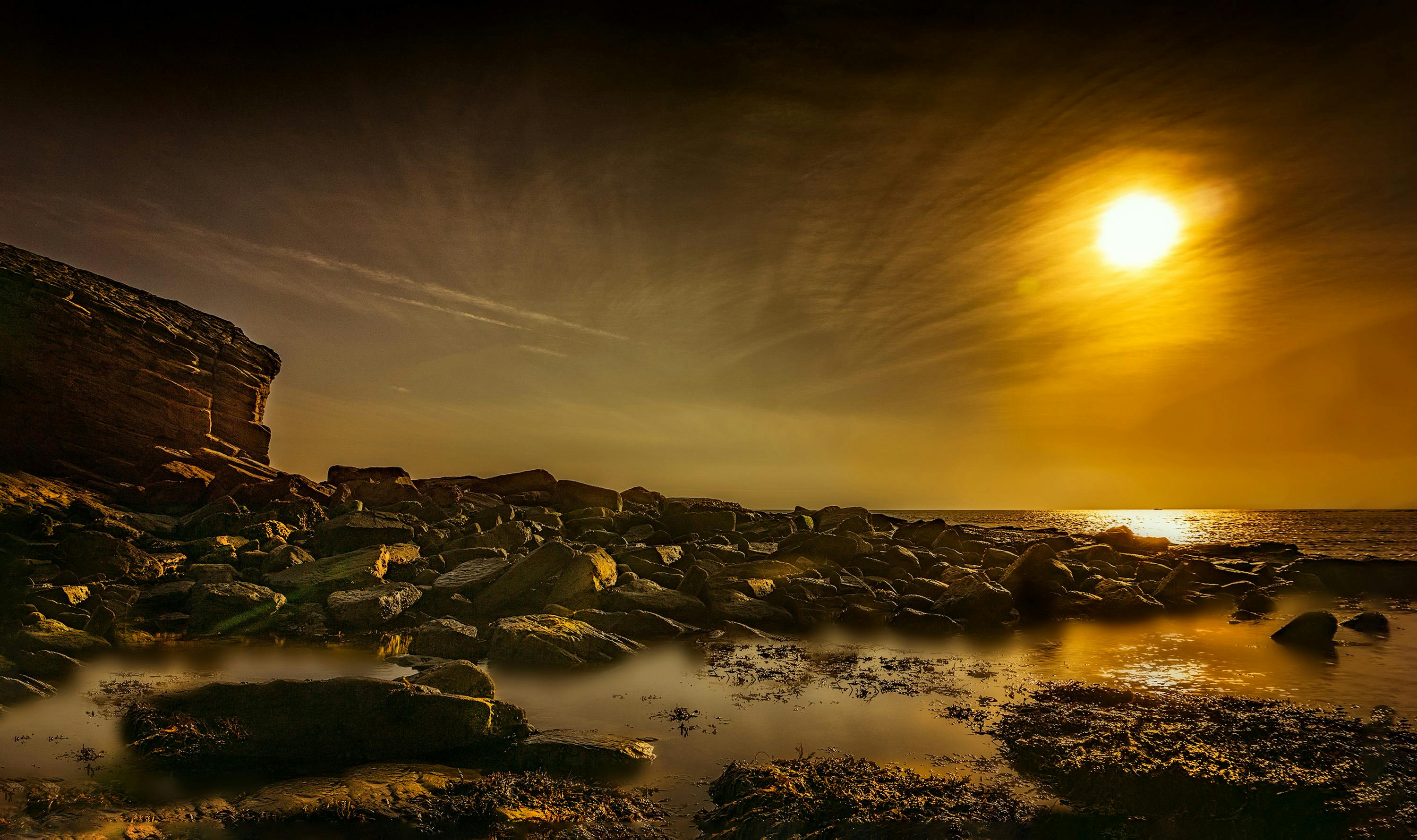 金色的日落映照着崎岖的岩石海岸，天空壮丽，水面平静