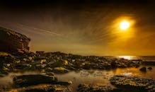 金色的日落映照着崎岖的岩石海岸，天空壮丽，水面平静