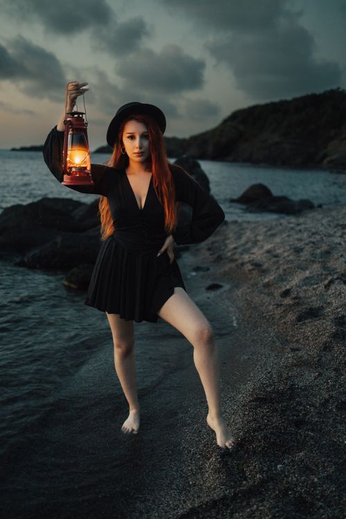 Free Moody portrait of a woman holding a lantern on the beach at dusk in Türkiye, capturing the sea and coastline. Stock Photo