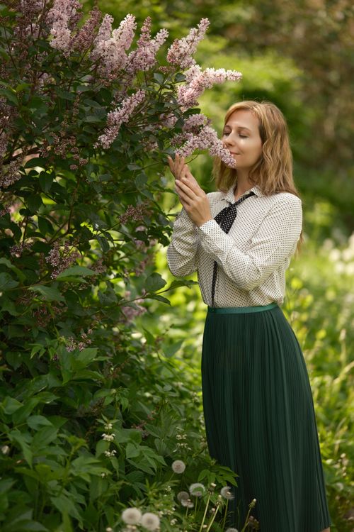 Free A woman in a garden gently touches and smells blooming lilac flowers, surrounded by lush greenery. Stock Photo