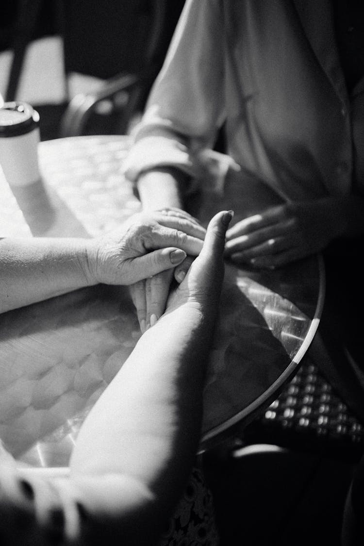 Close-up Of Mother And Daughter Holding Hands On A Table 