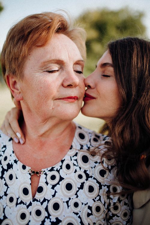 Free A tender moment of a woman kissing her mother on the cheek outdoors, symbolizing love and connection. Stock Photo