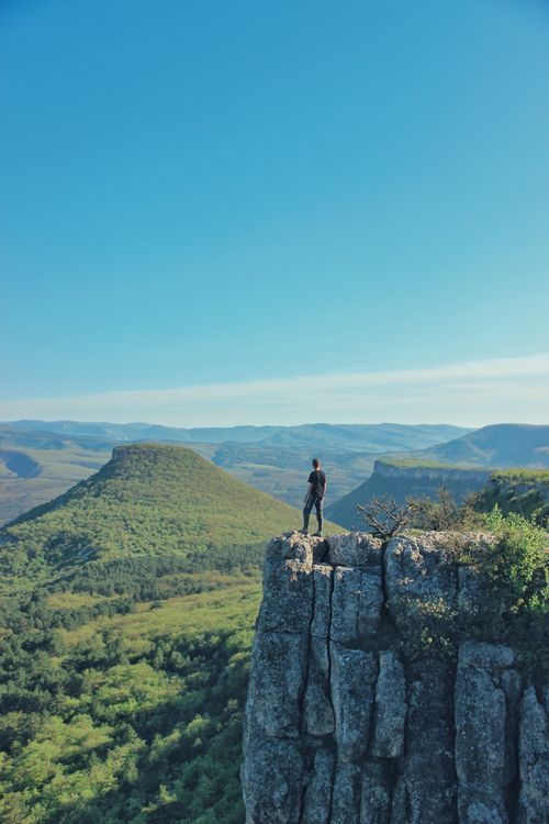 Free Man standing on a cliff with a panoramic view of lush mountains. Perfect for adventure and nature themes. Stock Photo