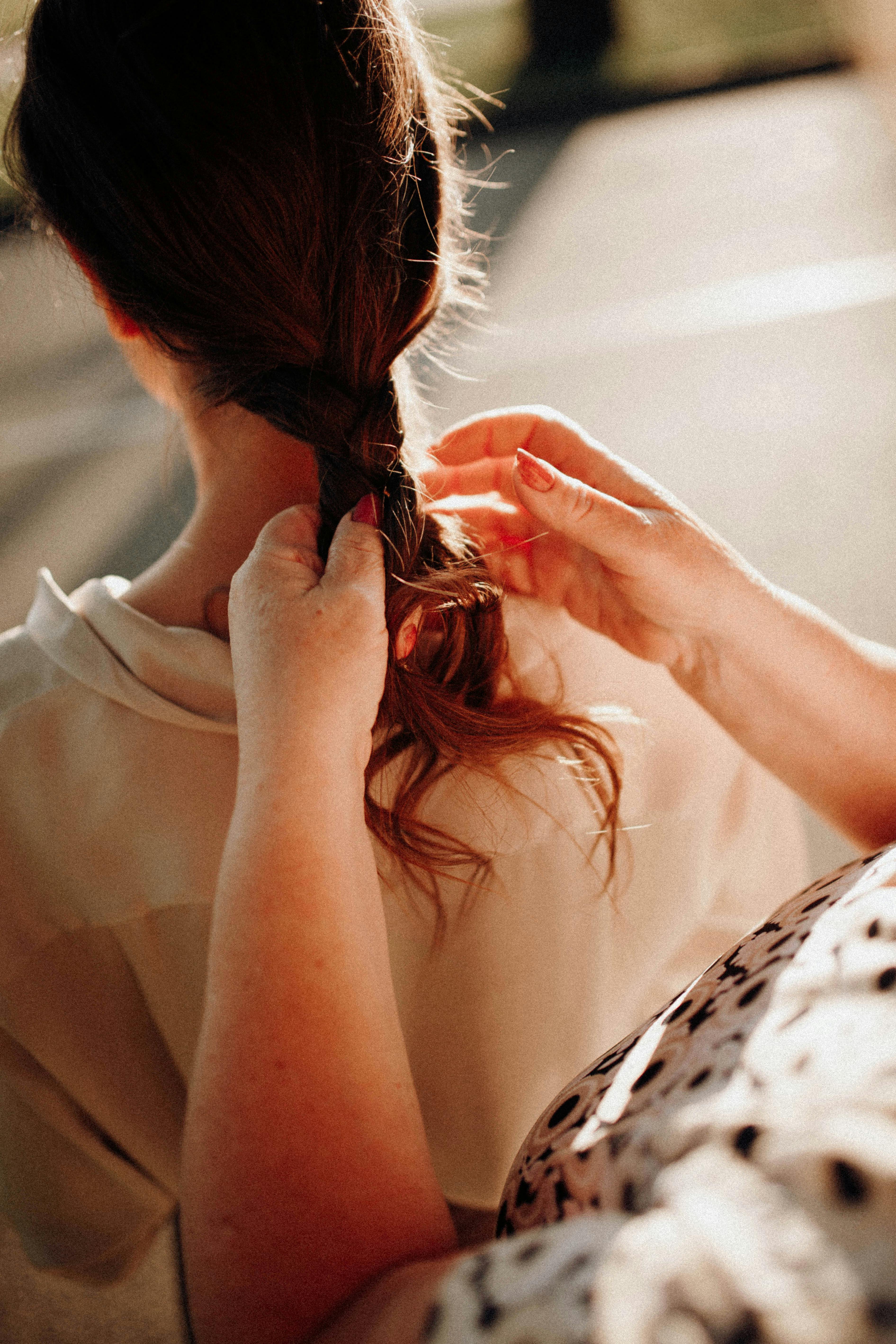 A mother tenderly braiding her daughter's hair in a warm outdoor setting.