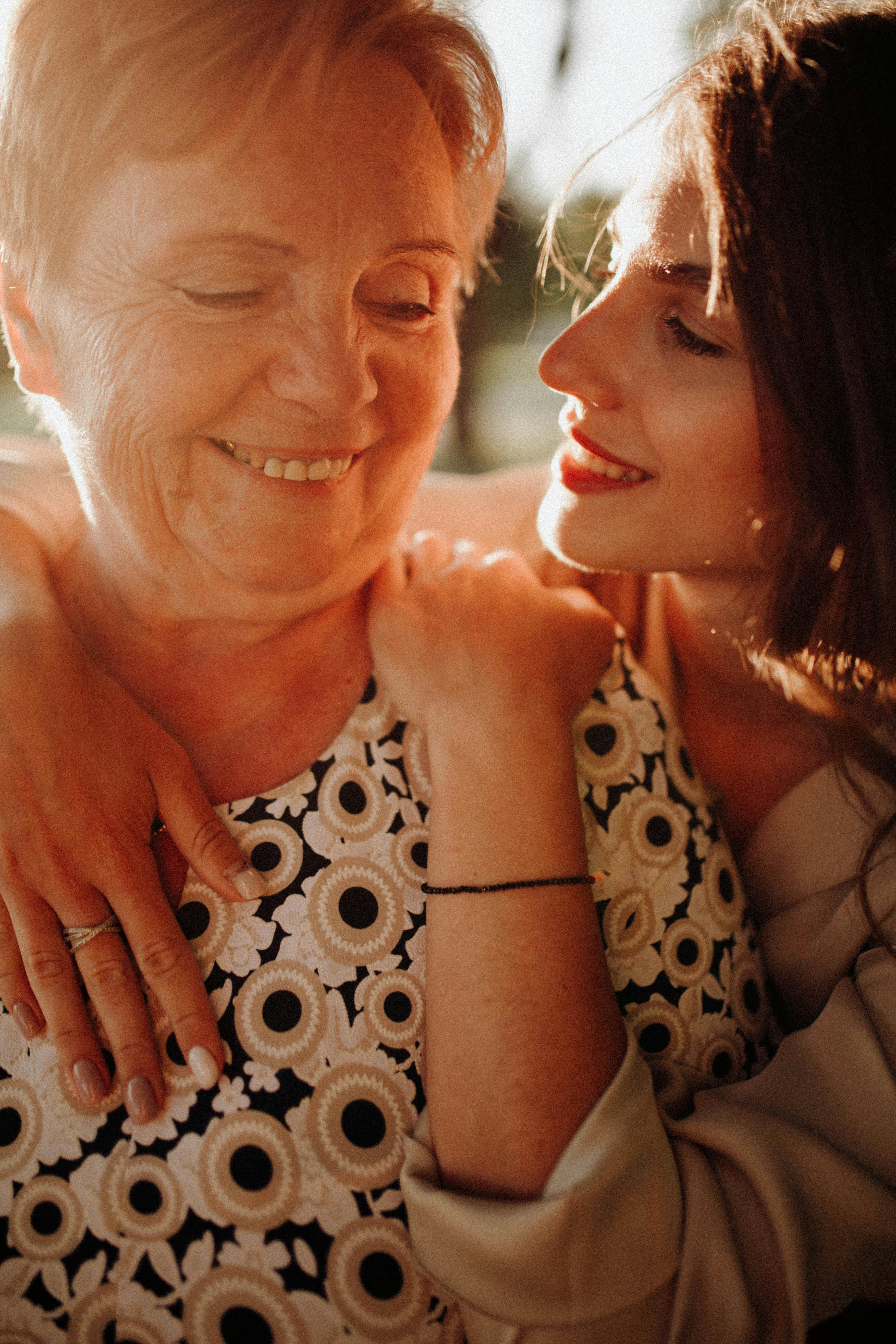 A warm moment of a mother and daughter embracing and smiling together outdoors.