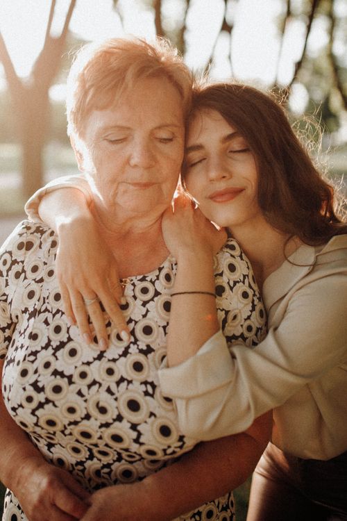 Free A heartwarming moment capturing a mother and daughter embracing outdoors in sunlight. Stock Photo