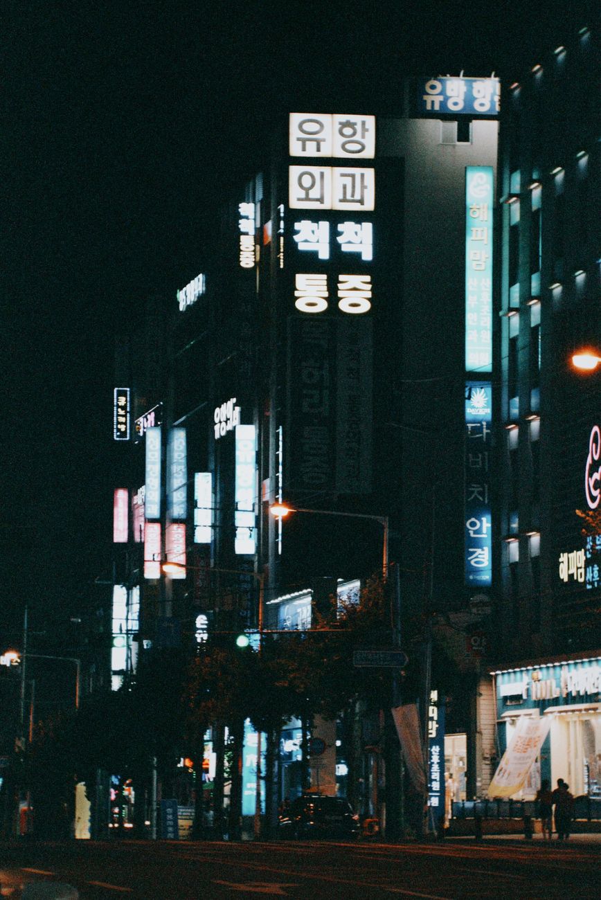 Illuminated city street in Cheongju-si, South Korea featuring modern architecture and vibrant signage.
