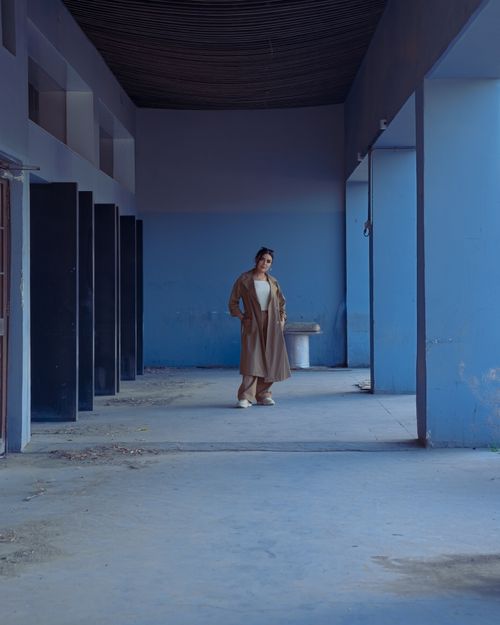 Free Fashionable woman in coat poses in urban corridor with blue walls, creating a modern and dramatic scene. Stock Photo