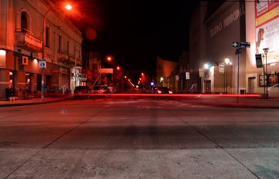 A tranquil urban street at night with illuminated buildings and light trails from moving vehicles.