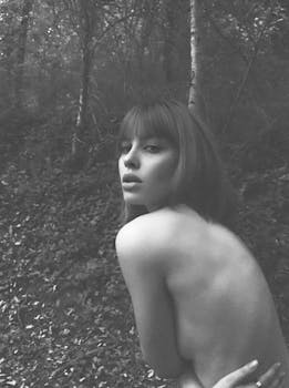 Expressive black and white portrait of a woman posing outdoors with forest backdrop.
