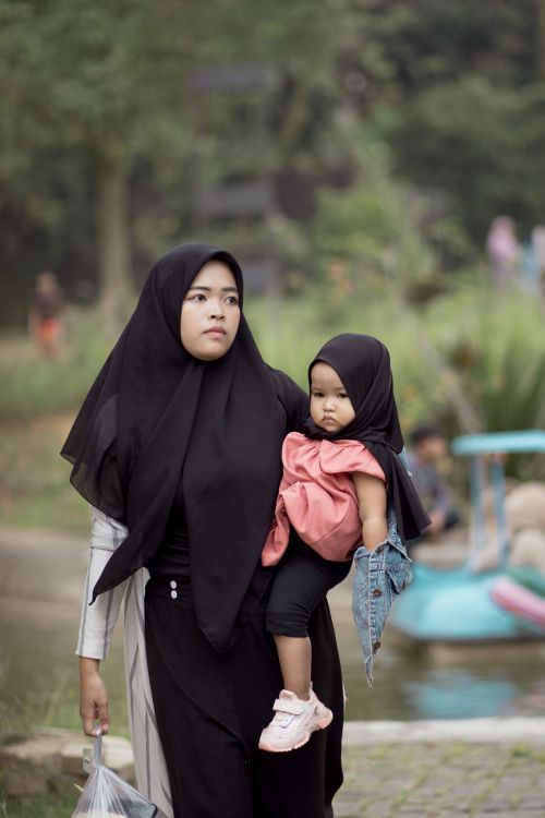 Free A mother with her child in hijabs walking near a park pond, expressing cultural attire. Stock Photo