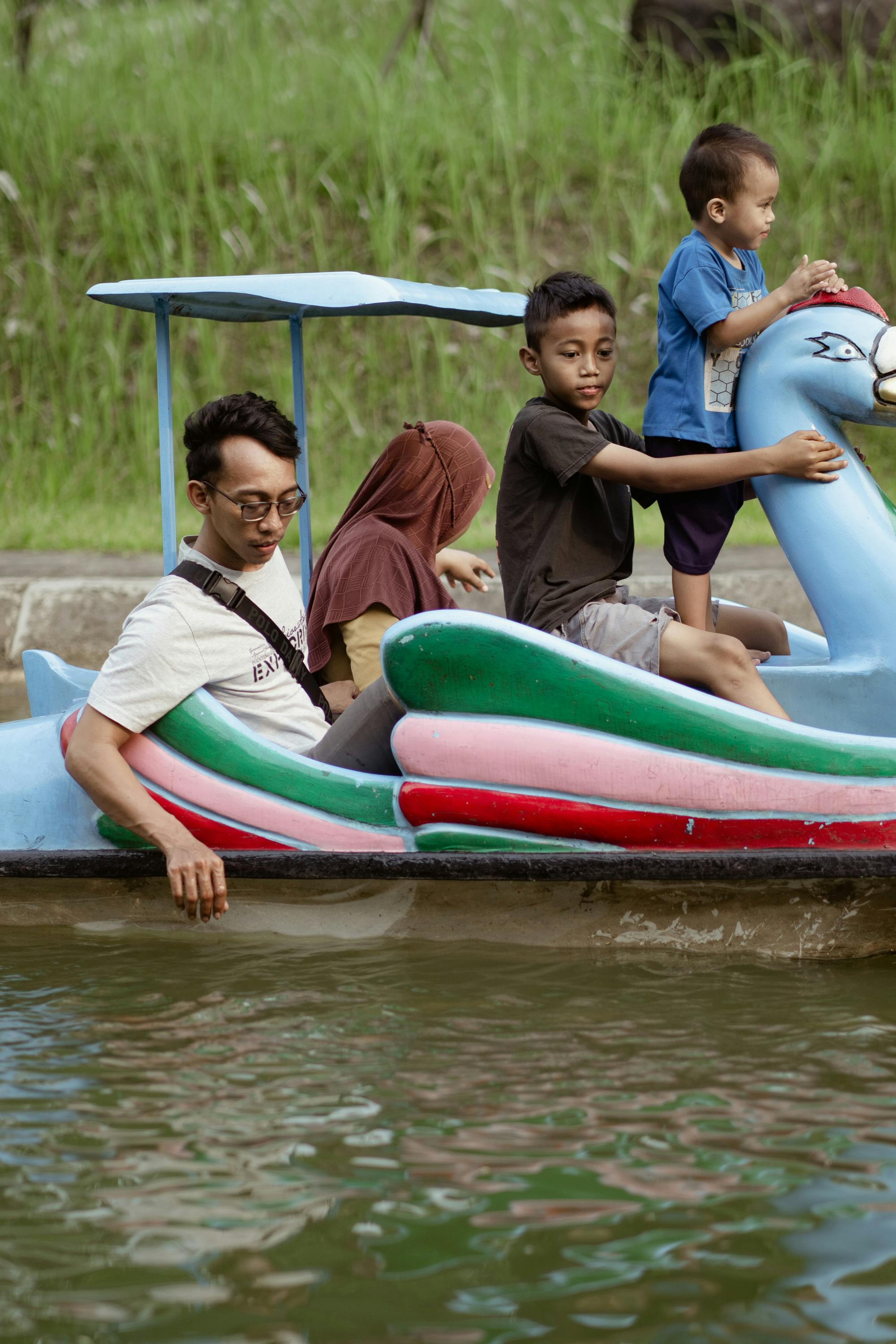 A family enjoys a leisurely afternoon on a colorful paddle boat in a serene park setting.