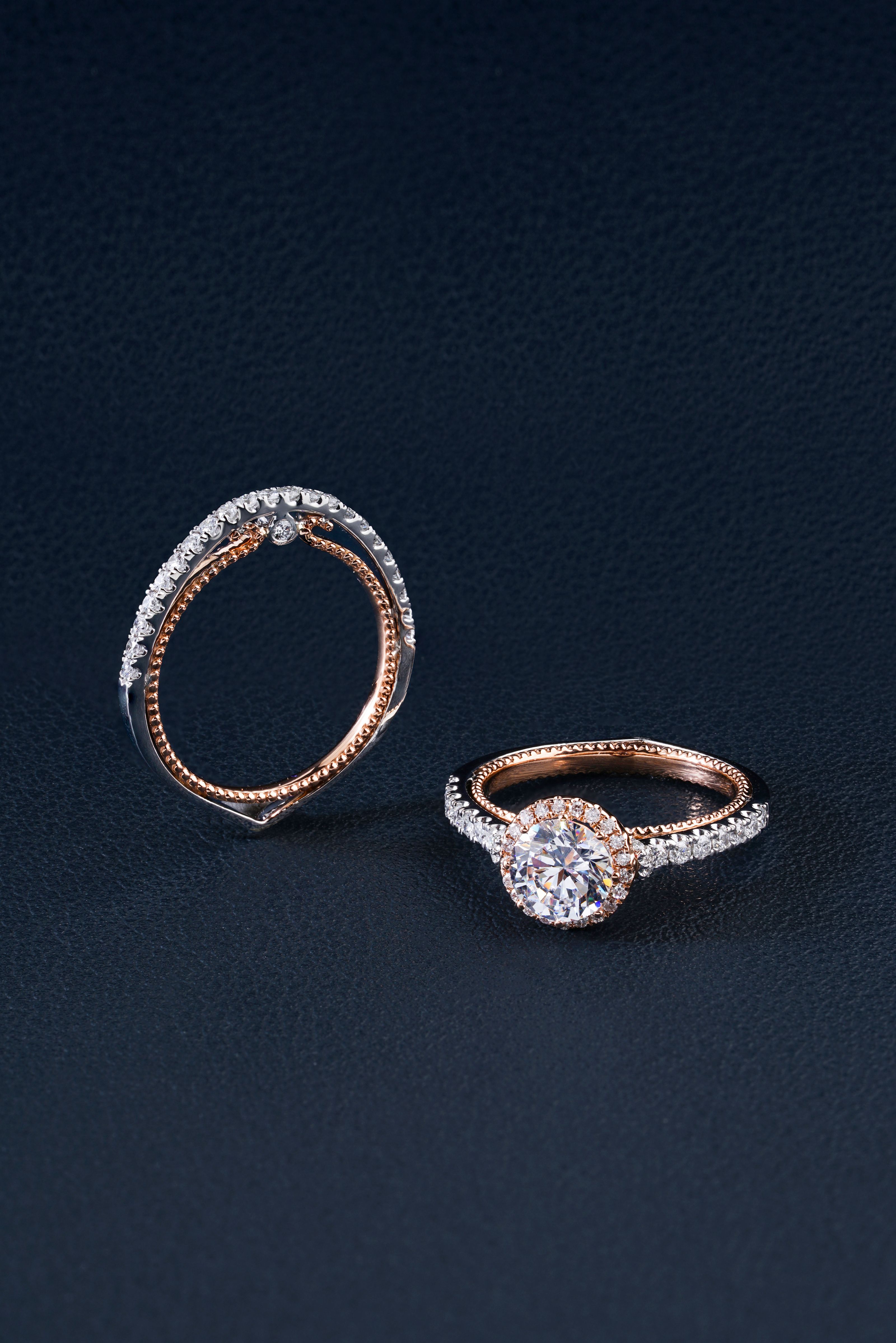 Conjunto estiloso de anéis de noivado e casamento em ouro rosa com diamantes sobre um fundo texturizado escuro.