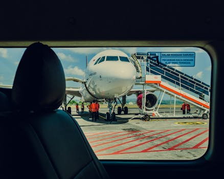 Airplane viewed from a car, parked on the tarmac at an airport with crew working nearby.