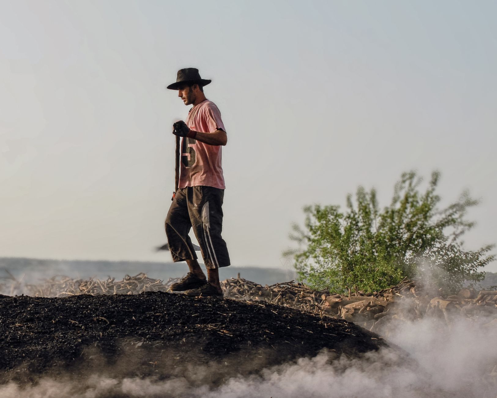 A man with a hat stands on a smoky terrain under the summer sun.