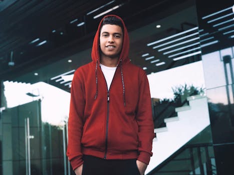 一位穿着红色连帽衫的时尚年轻人在城市环境中摆出户外姿势