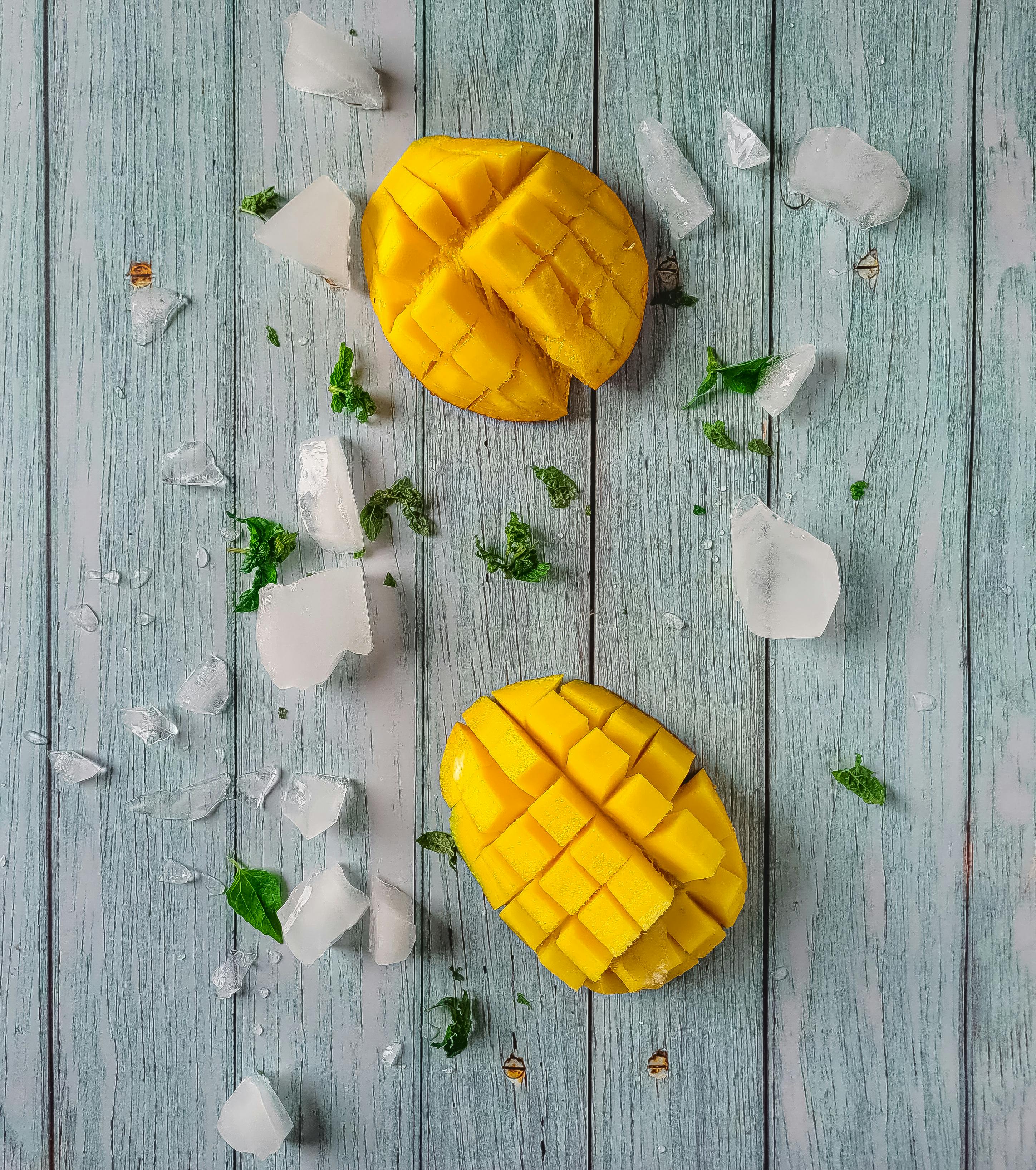 Juicy mango slices with ice and mint on a rustic table, perfect for summer vibes.