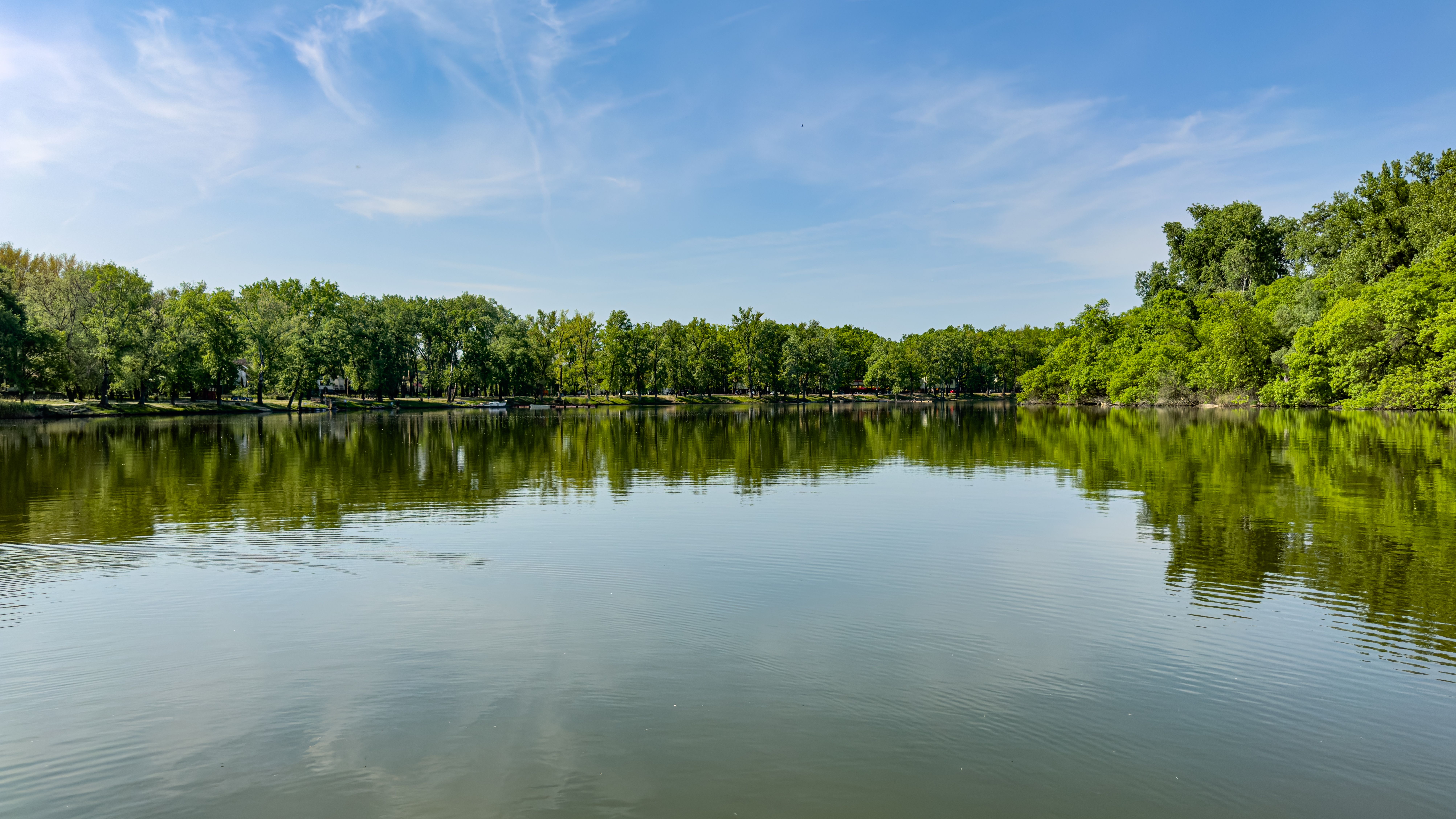 Serene landscape featuring a peaceful lake reflecting lush green trees under a clear blue sky.