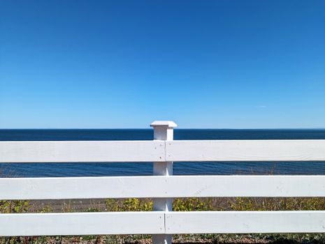 Serene view of a white wooden fence facing the ocean under a clear blue sky in summer.